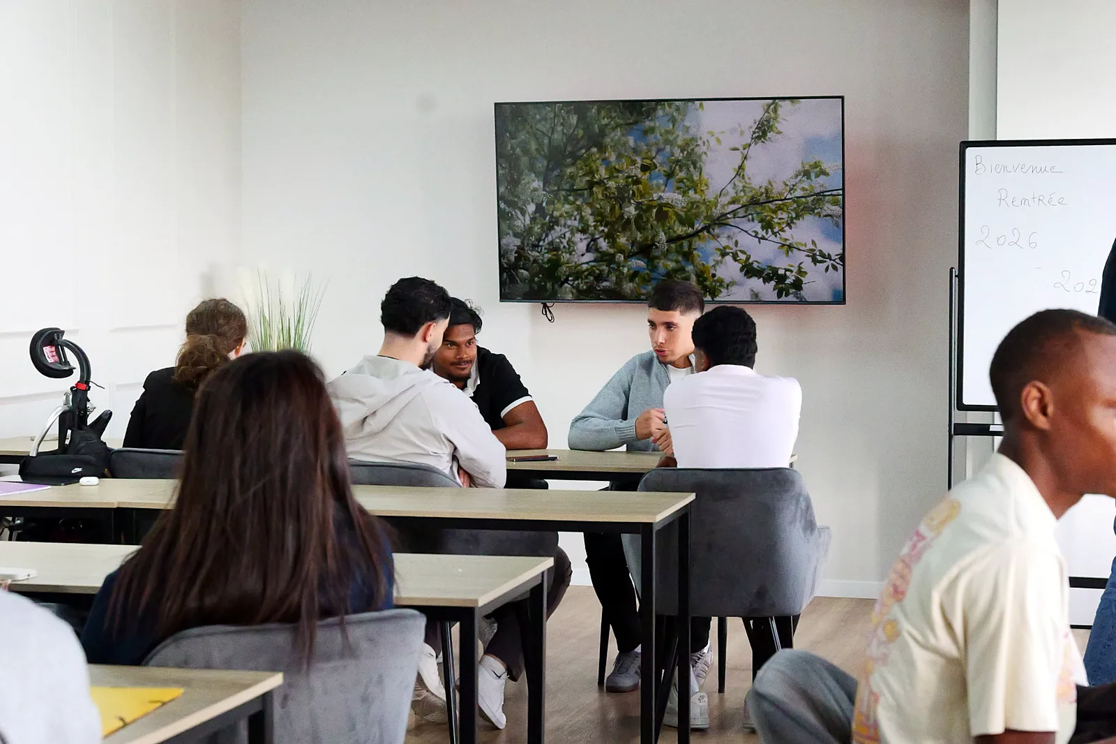 Des apprenants discutent par petits groupes dans une salle de cours lumineuse