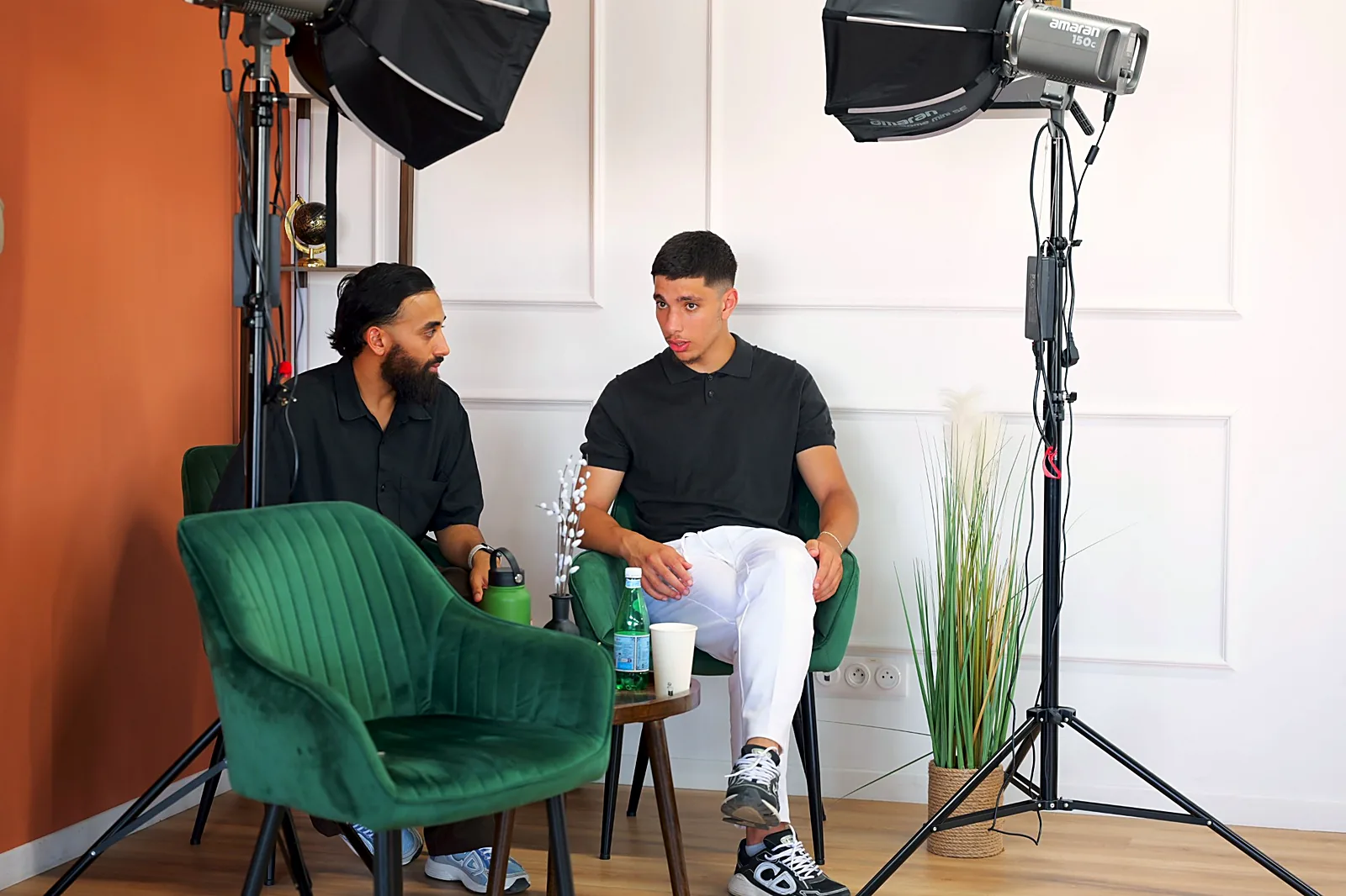 Deux personnes échangent dans le studio podcast, entre fauteuils verts et projecteurs